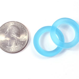K&ouml;nnte beinhalten: Zwei hellblaue, gefrostete Glasringe, einer etwas gr&ouml;&szlig;er als der andere, liegen &uuml;bereinander. Die Ringe sind etwa so gro&szlig; wie eine US-amerikanische 25-Cent-M&uuml;nze.
