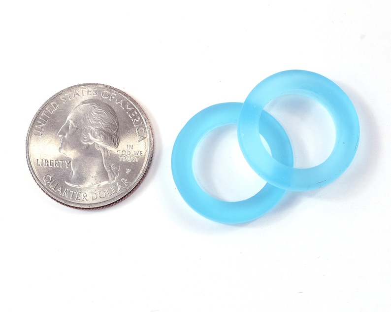 K&ouml;nnte beinhalten: Zwei hellblaue, gefrostete Glasringe, einer etwas gr&ouml;&szlig;er als der andere, liegen &uuml;bereinander. Die Ringe sind etwa so gro&szlig; wie eine US-amerikanische 25-Cent-M&uuml;nze.
