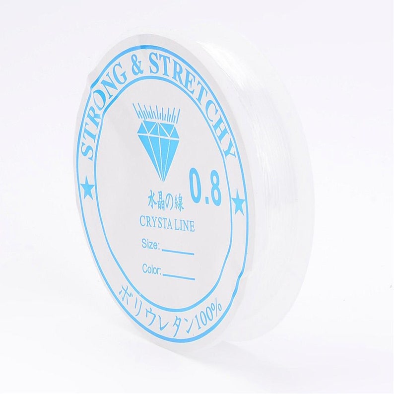 Op de afbeelding: Een spoel met helder elastisch garen met het label "STRONG & STRETCHY", een diamantlogo en de tekst "水晶の後 0.8 CRYSTA LINE Size: Color. ポリウレタン100%"