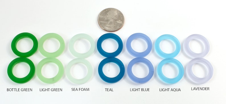 K&ouml;nnte beinhalten: Acht Glasringe in verschiedenen Gr&uuml;nt&ouml;nen, Blau- und Lilat&ouml;nen. Die Ringe sind von links nach rechts in einer Reihe angeordnet, wobei die Farben allm&auml;hlich von Gr&uuml;n nach Lila &uuml;bergehen. Die Ringe sind alle gleich gro&szlig; und gleich geformt und bestehen alle aus klarem Glas. Die Farben sind unter den Ringen beschriftet: Flaschengr&uuml;n, Hellgr&uuml;n, Meeresschaum, Teal, Hellblau, Hellblau, Lavendel.