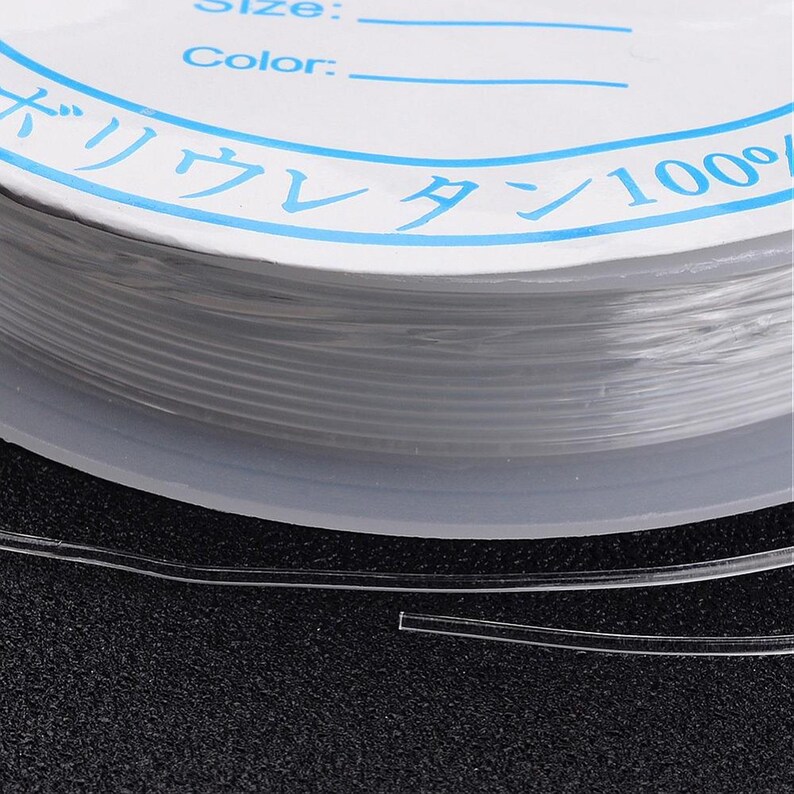 Op de afbeelding: Een spoel met heldere elastische draad met een wit label waarop "Grootte:" en "Kleur:" staat, en in het Japans "バリカレタン100%"