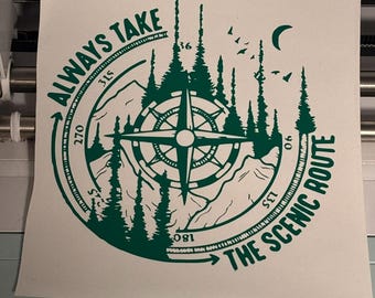 Puede incluir: Pegatina de vinilo verde con un diseño de brújula, montañas, árboles y el texto "ALWAYS TAKE THE SCENIC ROUTE". El diseño incluye una luna creciente y pájaros. La pegatina está sobre un fondo blanco.