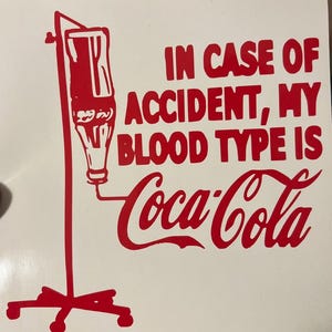 Puede incluir: Gráfico rojo sobre fondo blanco. El texto dice "EN CASO DE ACCIDENTE, MI GRUPO SANGUÍNEO ES Coca-Cola" con una ilustración de una bolsa de goteo intravenoso. El logotipo de Coca-Cola está en la escritura clásica.