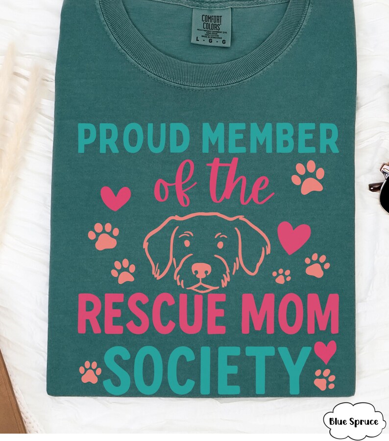 May include: Teal Comfort Colors t-shirt with the text "PROUD MEMBER of the RESCUE MOM SOCIETY" in teal and pink. The design includes a dog illustration, hearts, and paw prints.