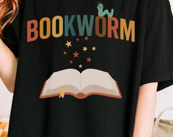 May include: Black t-shirt with the word "BOOKWORM" in colorful letters, a green worm wearing glasses, and an open book illustration. Gold and red stars are scattered above the book. The shirt is a casual style.