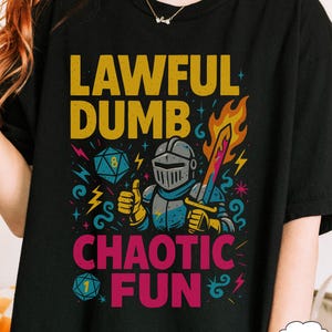 May include: Black t-shirt with a colorful graphic featuring a knight in armor, a flaming sword, and dice. The text reads "LAWFUL DUMB CHAOTIC FUN" in yellow and pink, with lightning bolt and star accents.