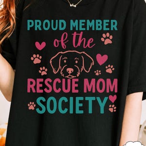 May include: Black t-shirt with the text "PROUD MEMBER of the RESCUE MOM SOCIETY" in teal and pink. The design includes a dog outline, paw prints, and hearts.