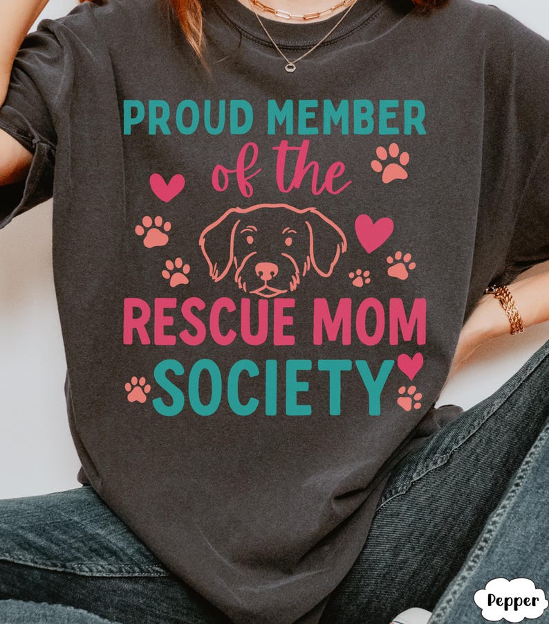 May include: Dark gray t-shirt with the text "PROUD MEMBER of the RESCUE MOM SOCIETY" in teal and pink. The design includes paw prints, hearts, and a dog illustration.