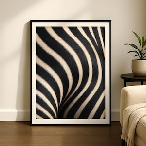 Op de afbeelding: Een ingelijste kunstdruk met een close-up van zebra strepen. Het zwart-witte patroon creëert een gebogen, getextureerd ontwerp. Het kunstwerk wordt gepresenteerd in een zwart frame, wat een moderne touch toevoegt aan de dierlijke beelden.