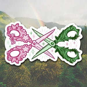 Puede incluir: Un par de tijeras adornadas con un diseño rosa y verde. Las tijeras están cruzadas y tienen un patrón floral con estrellas. El fondo es una imagen borrosa de un bosque.