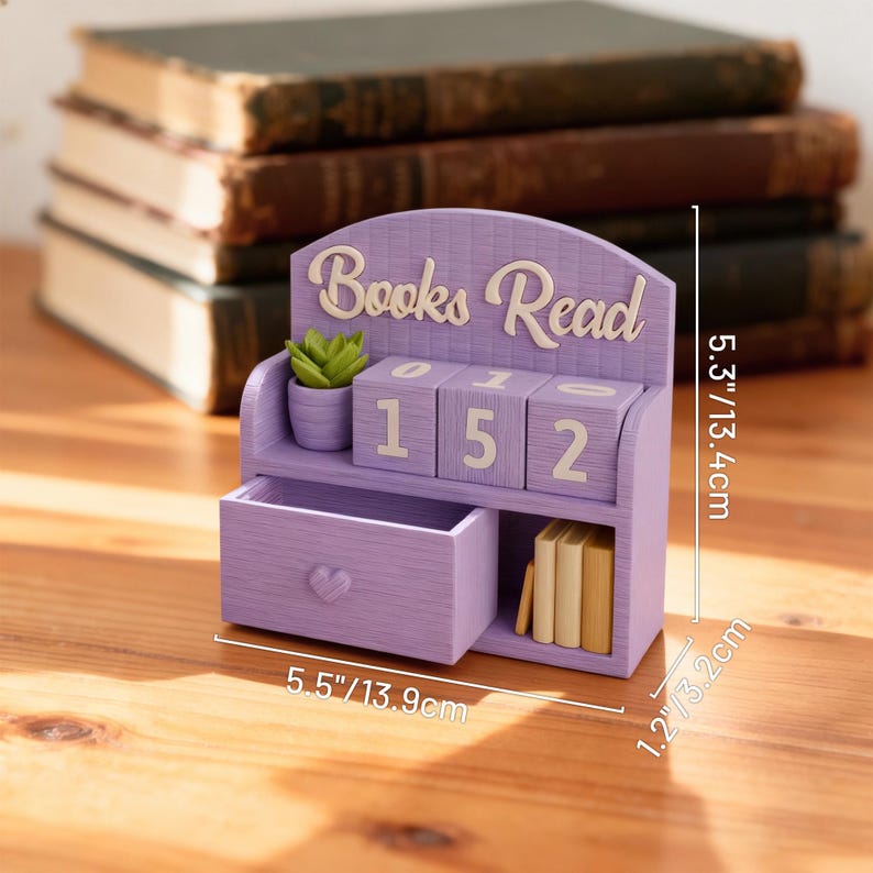 May include: A lavender-colored wooden bookshelf with the words "Books Read" on top. It features a small drawer, a miniature succulent, and numbered blocks displaying "152". The bookshelf is 5.5 inches wide, 5.3 inches tall, and 1.2 inches deep.