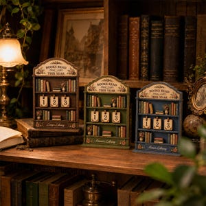 May include: Three wooden bookshelf-shaped trackers labeled BOOKS READ THIS YEAR with numbered cards 1, 2, and 3. Each unit features miniature book spines, floral accents, and a personalized name plate reading Lucy's Library, Emma's Library, or Anna's Library.