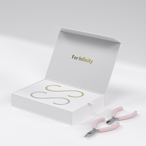 May include: White box with the words "For Infinity" on the lid. Inside the box are three gold and silver infinity symbol chains. Two pink pliers are next to the box.