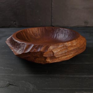 May include: A hand-carved wooden bowl. The bowl has a rough, textured exterior and a smooth interior. The bowl is a rich, warm brown colour, showcasing the natural wood grain. The bowl is likely used for serving or display.