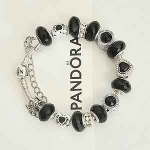 May include: A white ceramic mug with a black handle and the text "But First, Coffee" in a bold, black font. The mug is set against a blurred background, suggesting a cozy setting.