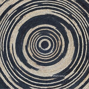 May include: Round jute rug with a spiral design. The rug features alternating concentric circles of navy blue and natural beige. The texture of the rug is visible, with the text "2025 Etty" in the lower right corner.