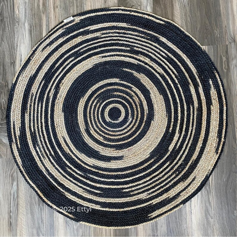 May include: A round jute rug with a concentric spiral design. The rug features alternating bands of navy blue and natural beige, creating a bold, eye-catching pattern. The rug is suitable for indoor use.