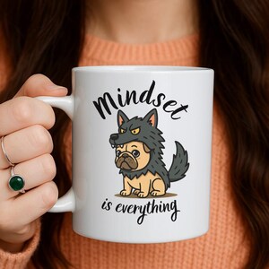 May include: White ceramic mug featuring a cartoon pug wearing a wolf costume. The mug has the words "Mindset is everything" in black script. The pug is tan and the wolf costume is gray.