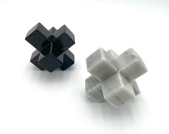 May include: Two decorative stone sculptures. One is black and the other is white with gray veining. Each sculpture is a geometric shape composed of interlocking cubes. The objects are displayed on a white surface.