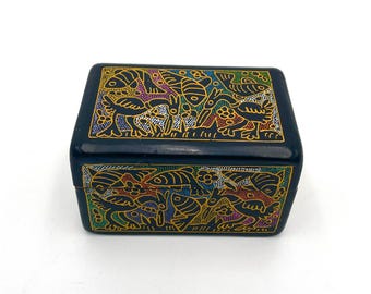 May include: A small, dark blue box with a rectangular shape. The box is adorned with a gold-outlined, colorful design featuring stylized birds, fish, and floral elements. The design is repeated on the top and sides.