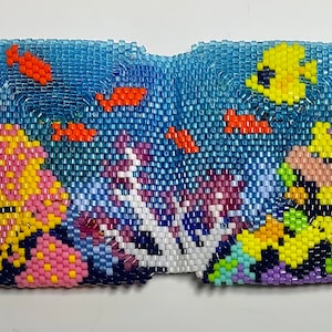 May include: A beaded wall hanging depicting an underwater scene with coral reefs, fish, and a yellow fish in the top right corner.