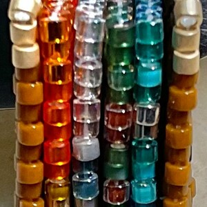 以下が含まれることがあります： 銀色の輪が付いた虹色のビーズキーホルダー。ビーズは縦に積み重ねられており、各色は虹の異なる部分を表しています。キーホルダーは小さな丸いビーズで作られています。