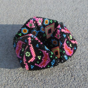 Pode incluir: Um bracelete de contas pretas com um padrão geométrico em rosa, azul, verde e laranja.