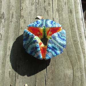 Könnte beinhalten: Ein farbenfroher, geometrischer Perlen-Schmuck mit einem blauen, grünen, roten und gelben Muster. Der Schmuck ist aus kleinen Perlen gefertigt und hat die Form einer Kugel.