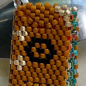 以下が含まれることがあります： 中央に黒い円形がある、小さな茶色のビーズチャーム。チャームは銀色のループに取り付けられており、カラフルなビーズの縁取りが施されています。