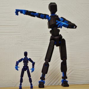 Op de afbeelding: Twee beweegbare actiefiguren, een grote en een kleine, in zwart en blauw. De grotere figuur heeft een arm uitgestrekt, de kleinere staat met gebogen armen. De figuren zijn ontworpen om poseerbaar te zijn, met meerdere gewrichten.