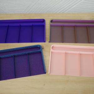 Può includere: Quattro organizer rettangolari nei toni del viola, marrone e rosa, ciascuno con quattro divisori verticali. Gli organizer sono in plastica e sono progettati per contenere piccoli oggetti.