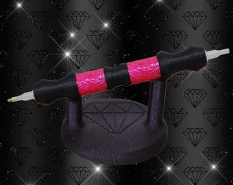 Puede incluir: Un bolígrafo de pintura de diamantes negro y rosa con un soporte a juego. El bolígrafo tiene un mango negro con detalles rosas y una punta blanca. El soporte es negro y presenta un diseño de diamante.