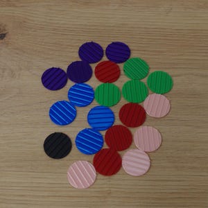 Puede incluir: Una colección de objetos circulares coloridos con superficies texturizadas. Los círculos son de varios colores, incluyendo azul con rayas blancas, rojo, verde, rosa, morado y negro. Los objetos están dispuestos sobre una superficie de madera marrón claro.