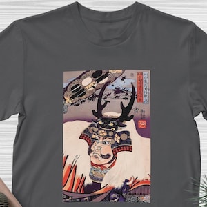 Puede incluir: Camiseta gris oscuro con una impresión japonesa en madera de un guerrero samurái. La obra de arte incluye el rostro del guerrero, su armadura y un fondo con caracteres japoneses.