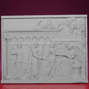 May include: A white relief sculpture depicting a classical scene with figures in flowing garments. The artwork features architectural elements, including a building with columns and a pediment, and a tree. The figures appear to be interacting in a narrative scene.