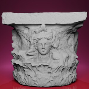May include: A gray, sculpted architectural element featuring a carved female face with flowing hair. The design is surrounded by textured, stylized foliage. The top of the element is a flat, rectangular shape.