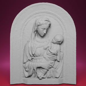 Può includere: Una scultura a rilievo di colore chiaro raffigurante una donna che tiene in braccio un bambino. La donna indossa un copricapo drappeggiato e un abito fluente. La scultura è ambientata in una cornice ad arco con un bordo decorativo, creando un'opera d'arte religiosa classica.