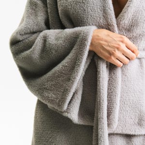 Puede incluir: Una bata gris suave con mangas anchas y un cintur&oacute;n a juego. El material de felpa tiene una textura borrosa. La bata est&aacute; envuelta alrededor del cuerpo, con el cintur&oacute;n atado a la cintura. La bata es de color neutro.