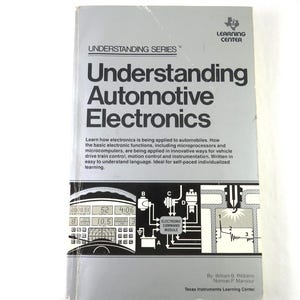 May include: A gray book titled "Understanding Automotive Electronics" by Texas Instruments Learning Center. The cover features the title in large, bold letters, with a diagram of electronic components. The book explains how electronics are applied to automobiles.