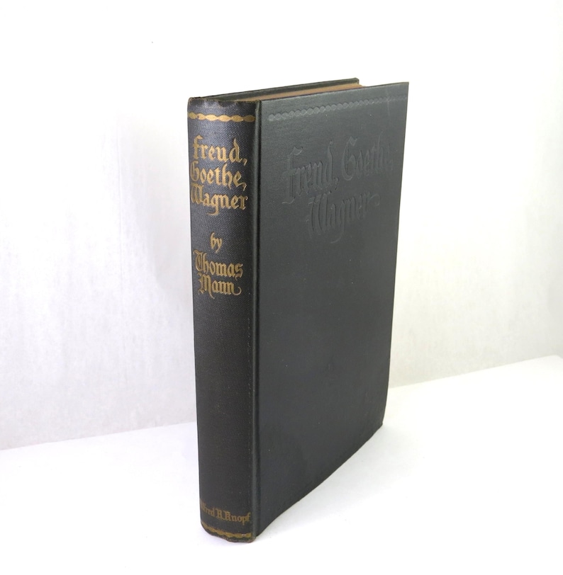 Może przedstawiać: Książka w twardej oprawie zatytułowana "Freud, Goethe, Wagner" autorstwa Thomasa Manna. Grzbiet jest ciemnobrązowy ze złotymi literami i elementami dekoracyjnymi. Okładka jest czarna z wytłoczonym tekstem.