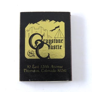 May include: A black matchbook with a gold design featuring a castle, mountains, and the text "Graystone Castle." The matchbook also includes the address "83 East 120th Avenue, Thornton, Colorado 80241."