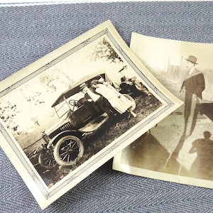 May include: Two vintage black and white photographs. One features a classic car with people, framed with an ornate border. The other shows a man in a hat, with a long shadow. Both are on a blue and white textured surface.