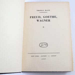 Może przedstawiać: Otwarta książka z tytułem "FREUD, GOETHE, WAGNER" autorstwa Thomasa Manna. Opublikowana w 1937 roku przez Alfred A. Knopf w Nowym Jorku. Zawiera małą, owalną ilustrację biegnącego psa.