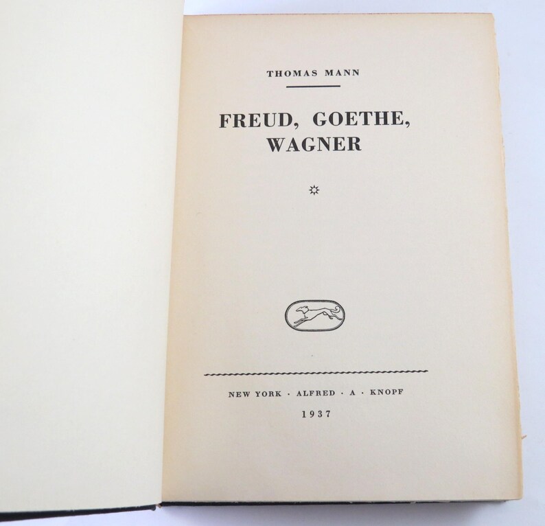 Może przedstawiać: Otwarta książka z tytułem "FREUD, GOETHE, WAGNER" autorstwa Thomasa Manna. Opublikowana w 1937 roku przez Alfred A. Knopf w Nowym Jorku. Zawiera małą, owalną ilustrację biegnącego psa.