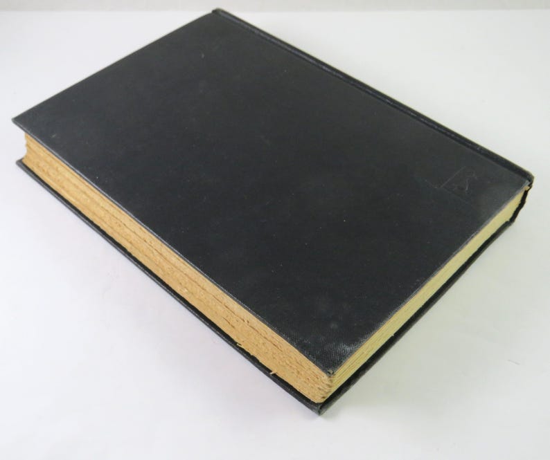 Może przedstawiać: Zamknięta książka w twardej oprawie z czarną okładką i poż&oacute;łkłymi, postarzanymi stronami. Grzbiet książki jest widoczny, a na okładce znajduje się mały, wytłoczony wz&oacute;r. Książka leży na białej powierzchni.