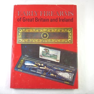 May include: A red book titled "EARLY FIREARMS of Great Britain and Ireland" with a detailed illustration of a gun case. The case is open, revealing a gun and accessories. The cover features a decorative gold and brown rectangular design.