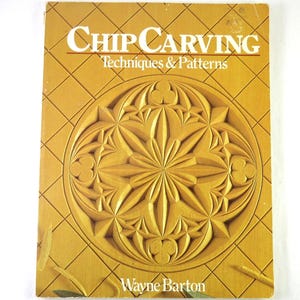 May include: A vintage book titled "Chip Carving Techniques & Patterns" by Wayne Barton. The cover features a detailed, carved floral design in shades of gold and brown, set against a grid pattern.