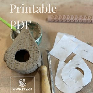 以下が含まれることがあります： 手作りの粘土製の鳥小屋。花柄模様、丸い開口部、そして「Printable PDF」の文字が特徴です。画像には、ツール、紙のテンプレート、そして「Chaos to Clay Ceramics & More」のロゴも写っています。