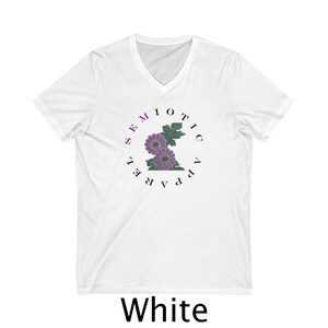 Peut inclure: T-shirt blanc à col en V avec le texte "SEMIOTIC APPAREL" dans un motif circulaire autour d'un motif floral violet. Le mot "White" est imprimé en bas du t-shirt.