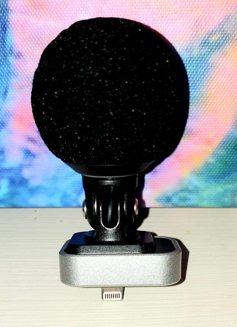 May include: A black microphone with a rounded, textured head, mounted on a black and silver base. The base has a silver rectangular body with a connector at the bottom. The background is a colorful, abstract design.
